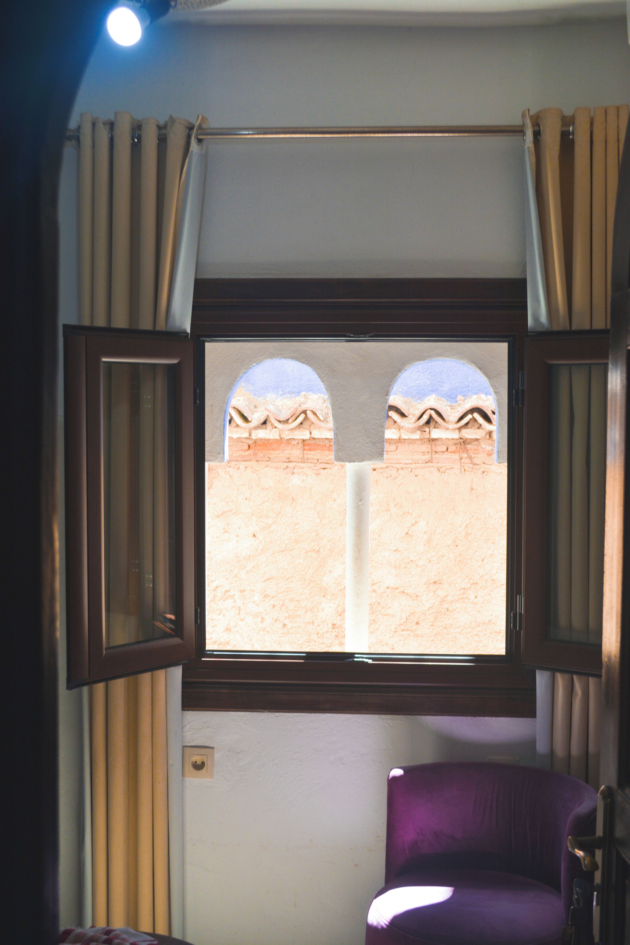 A room with a window, curtains, a chair, and a view of a brick wall.