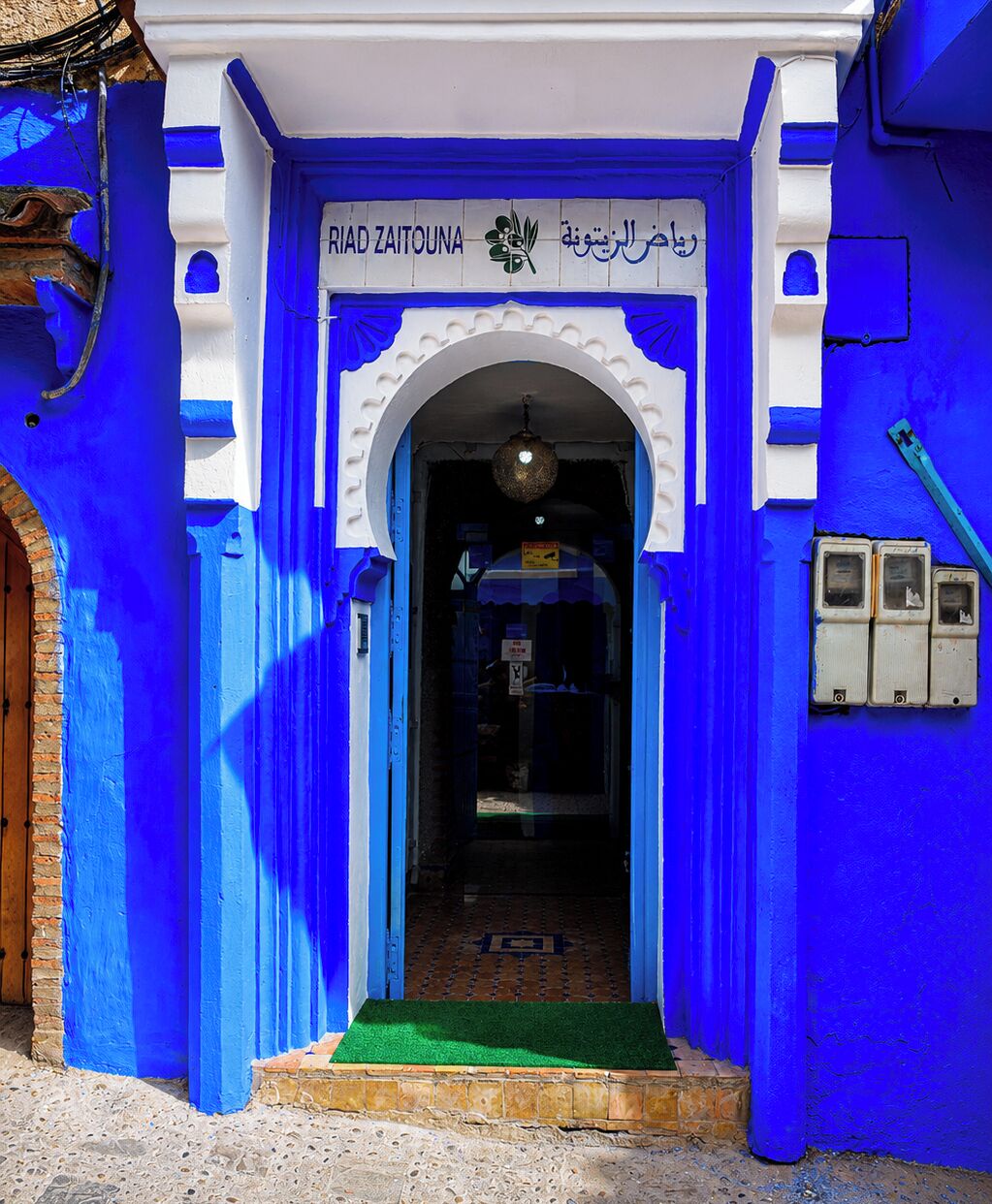 A building entrance with a blue facade, an archway, and a green mat at the entrance.