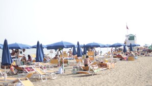 Ein Strand mit Reihen von Liegestühlen und Sonnenschirmen, einem Rettungsturm und entspannten Menschen.