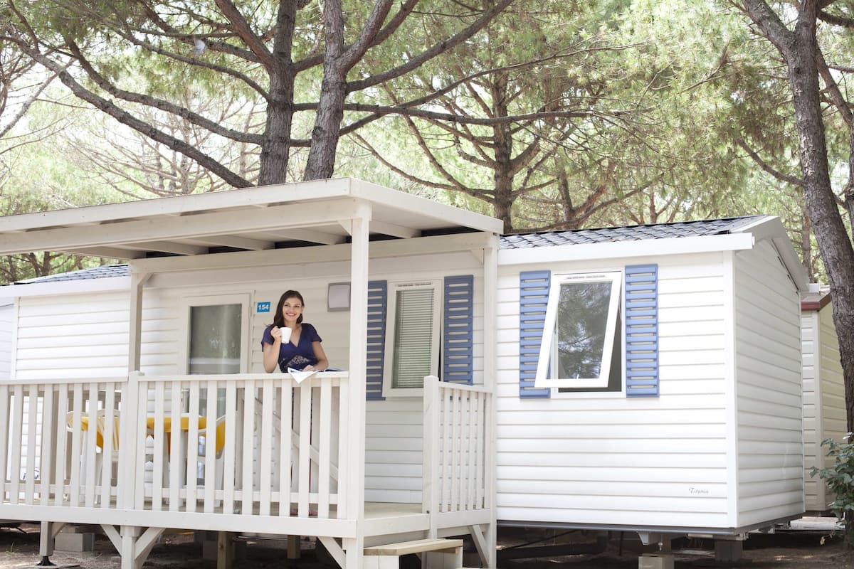 A white mobile home with blue shutters, a porch, and a number '154' sign.