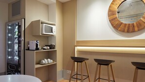 A modern kitchen with a built-in refrigerator, microwave, and a round mirror on the wall. There are three stools and a white table. - Hotel Berri Versalles (Renteria)