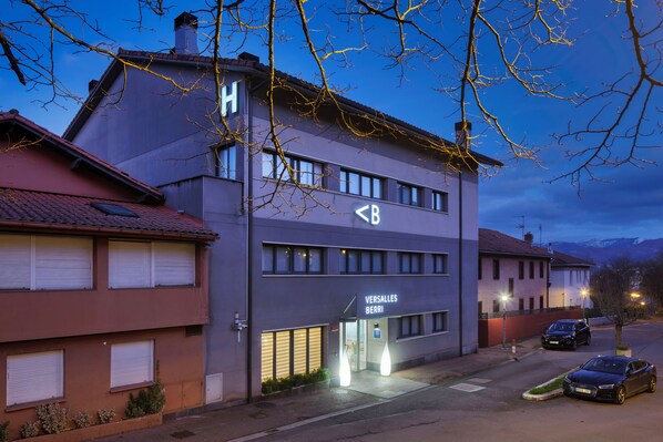 A modern building with a sign for 'Versalles Berri' and a parking area with cars.