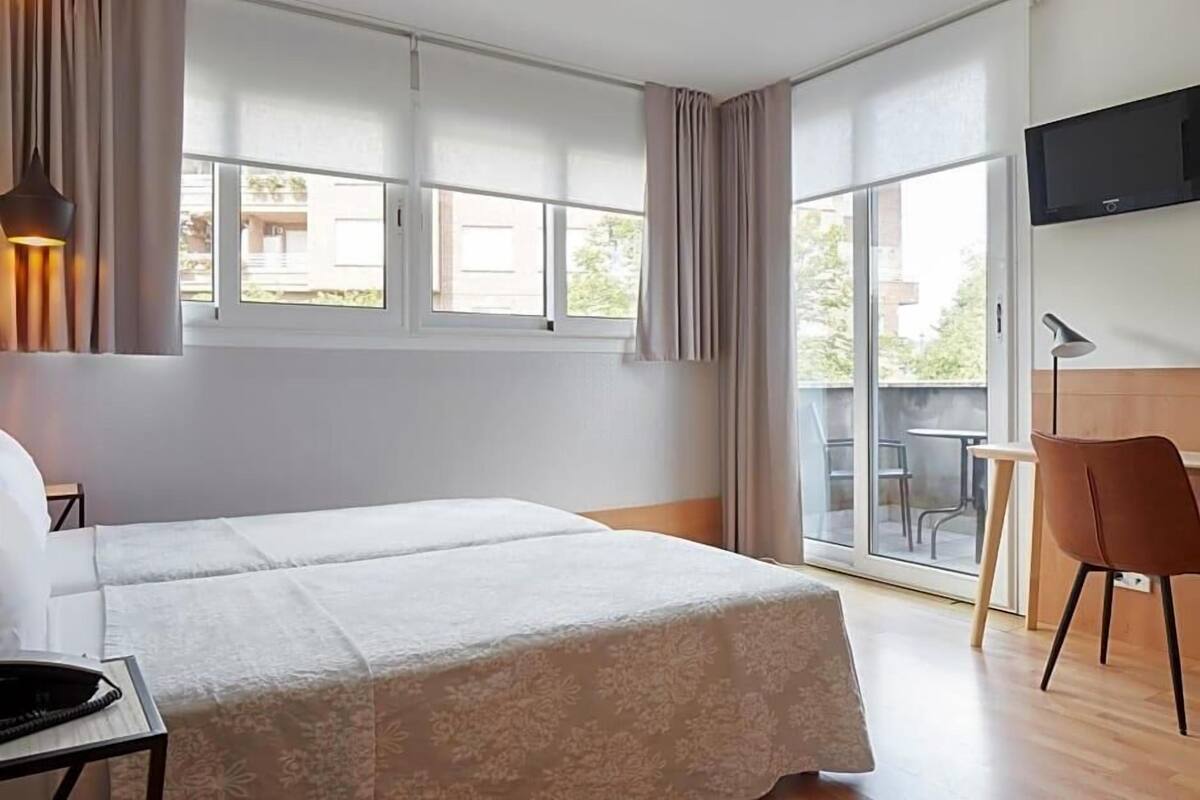 Habitación de hotel con cama, escritorio, silla, televisor y balcón con mesa y sillas.