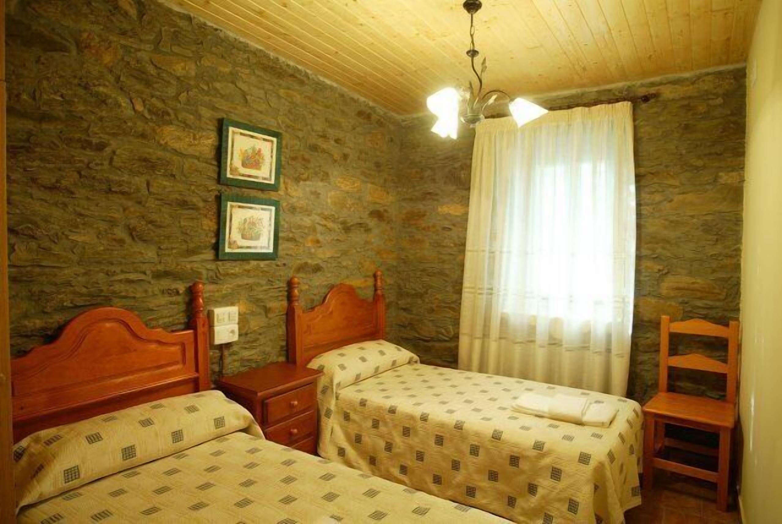 Ein Zimmer mit zwei Holzbetten, einer Steinwand, einer Holzbalkendecke und einem Fenster mit Vorhängen.