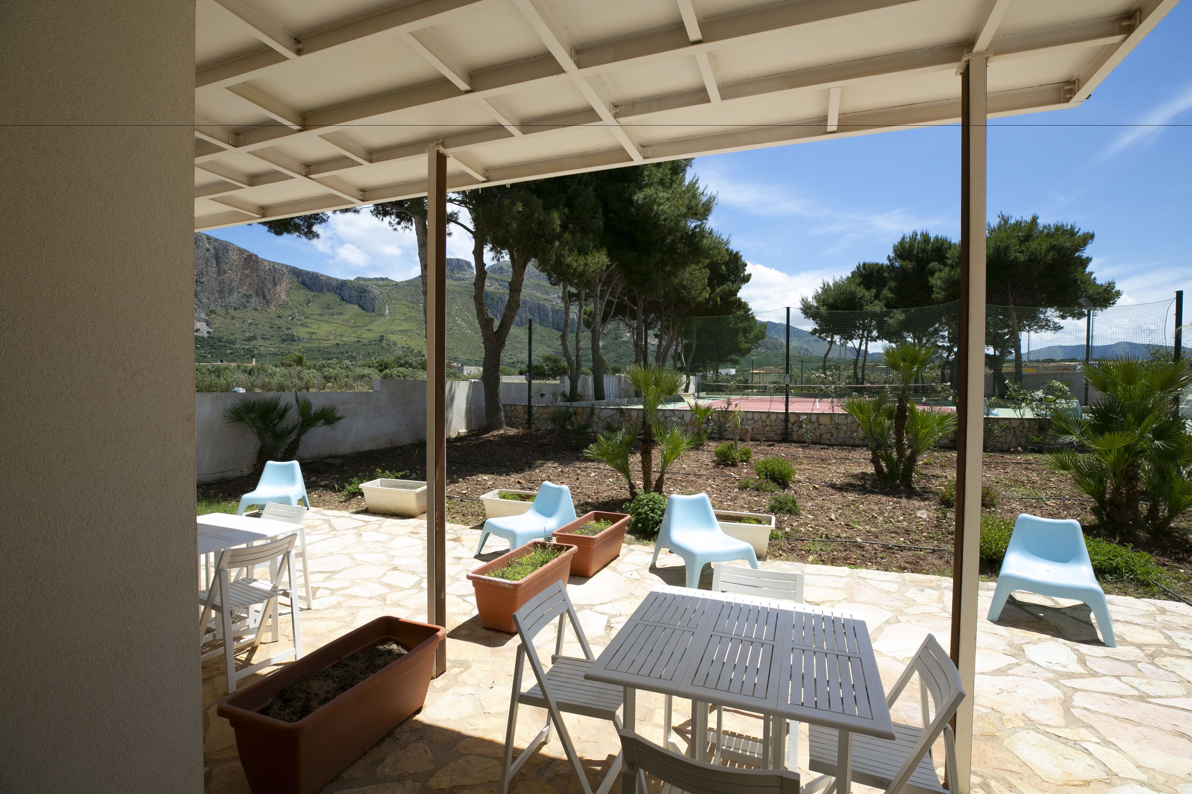 Un patio al aire libre con una mesa y sillas, rodeado de macetas y vistas a montañas.