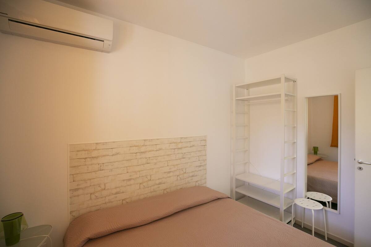 A bedroom with a bed, a white wardrobe, a mirror, and a green glass on a side table.