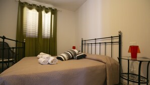 A neatly made bed with a striped pillow, rolled towels, and a red lamp on a small table beside it.