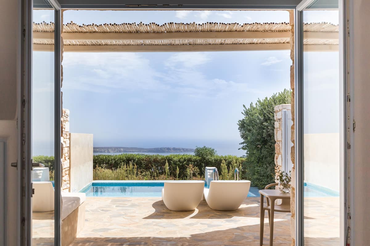 Un patio abierto con piscina, dos tinas blancas y vista al mar.