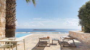 A stone patio with two lounge chairs and a table, overlooking a pool and the sea. - Calme Boutique Hotel Paros- Adults Only (Paros)