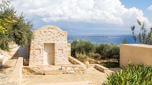 A stone building with a door, steps leading up to it, and a view of the sea in the background. - Calme Boutique Hotel Paros- Adults Only (Paros)