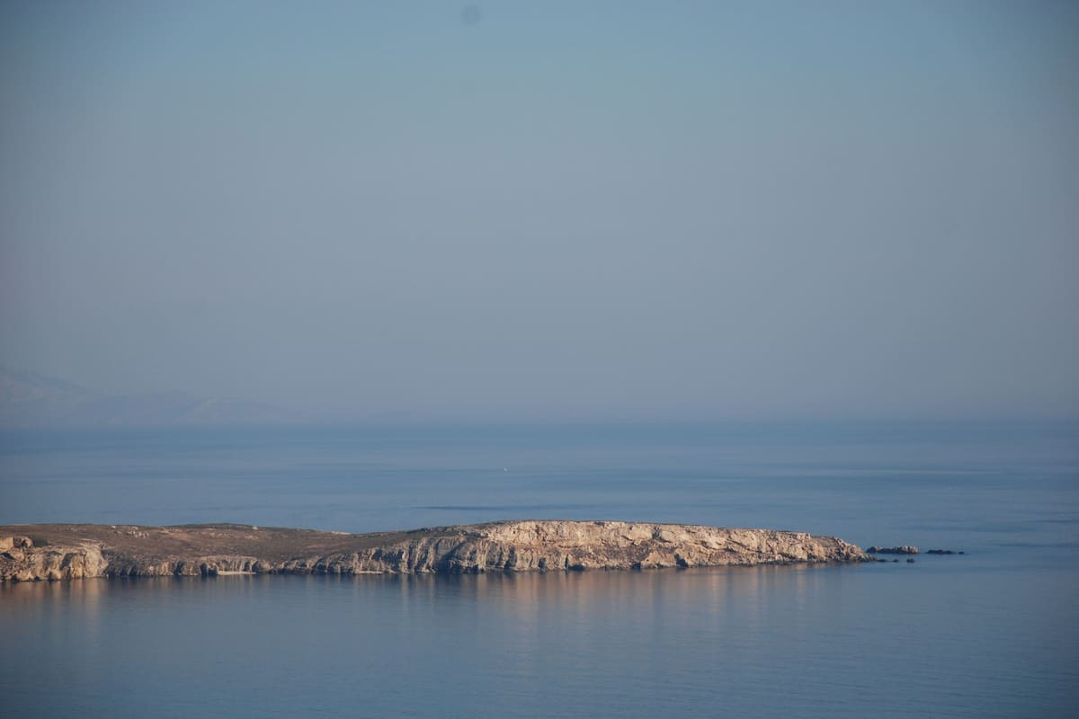 Un paisaje costero con un promontorio rocoso y mar tranquilo.