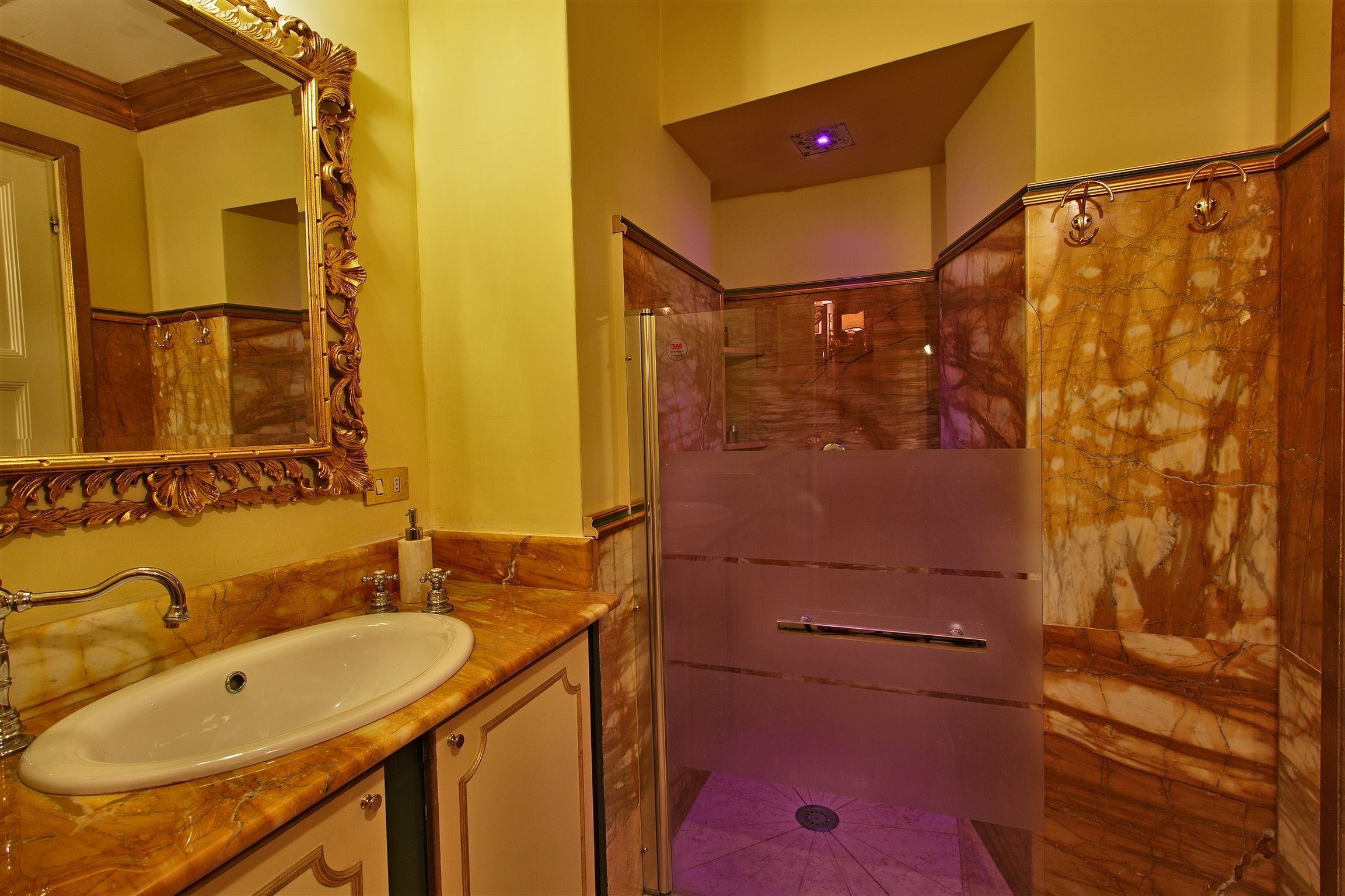 A bathroom with a marble sink, a large mirror, a shower with marble walls, and a door leading to another room.