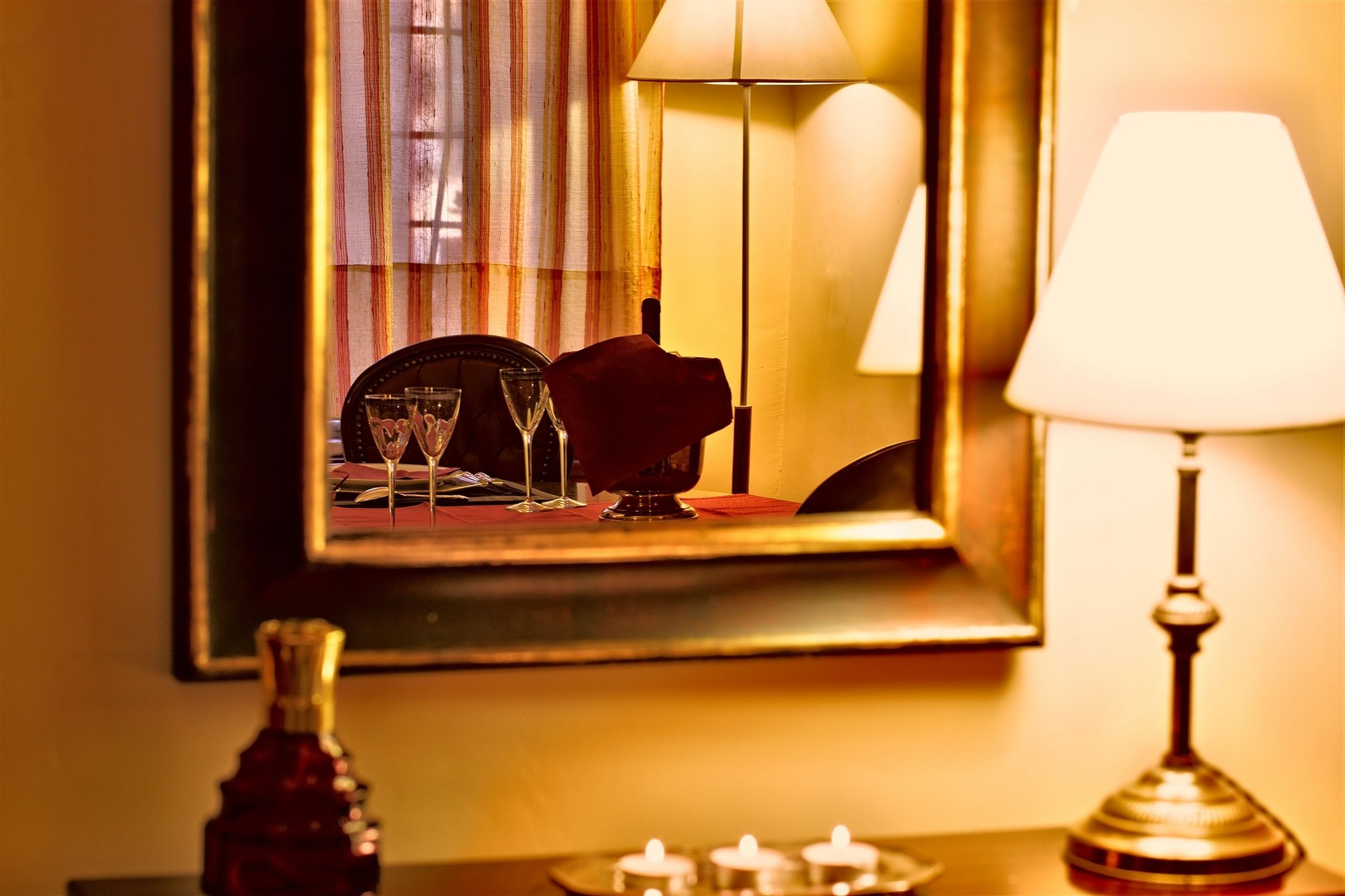 A mirror reflecting a dining table with a red rose, a bottle, and candles.