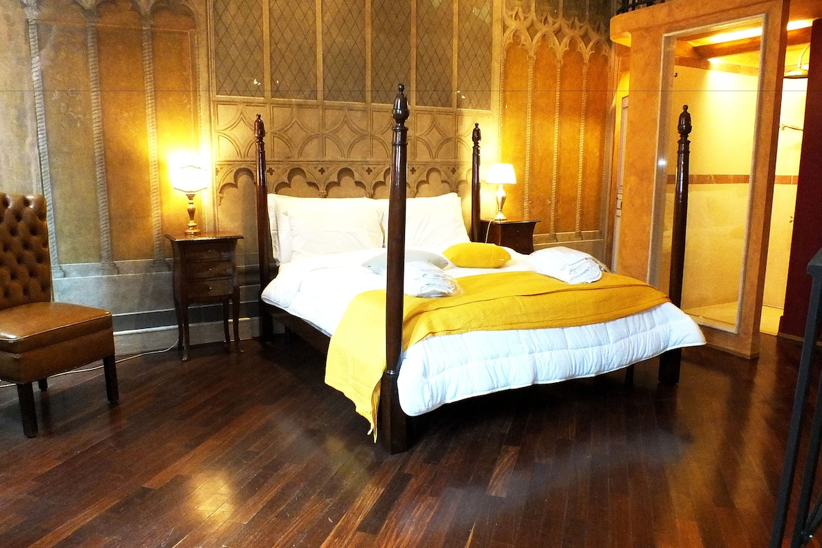 Una cama con dosel con un edredón amarillo, una silla de madera y una mesita de noche con una lámpara.