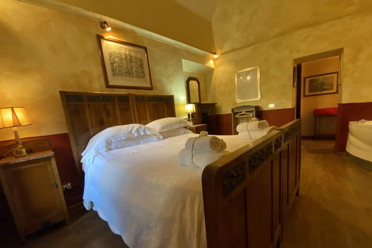 Una habitación de hotel con una cama de madera, una mesita de noche con lámpara, un espejo y un armario.