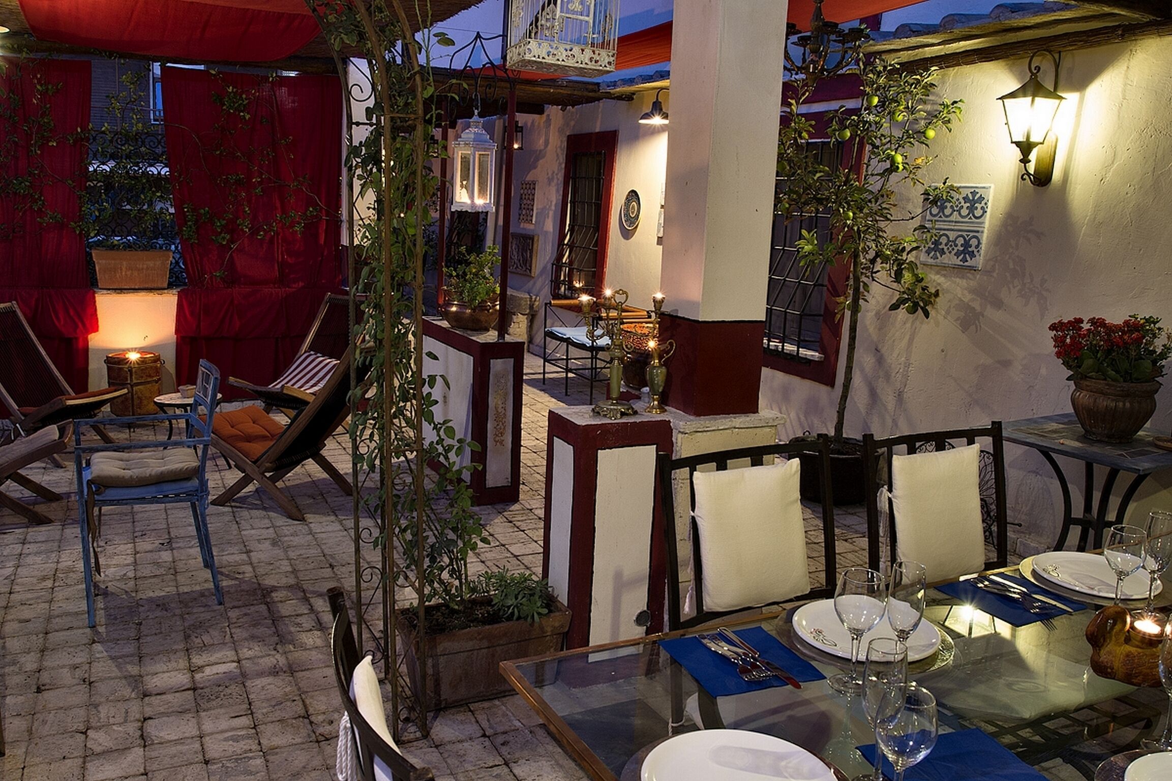 An outdoor dining area with tables set for two, surrounded by chairs and potted plants.