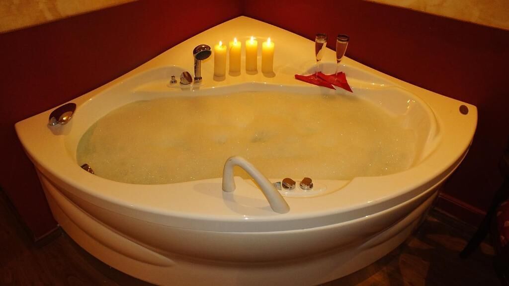 A bathtub with multiple candles, a red rose, and a glass of water.