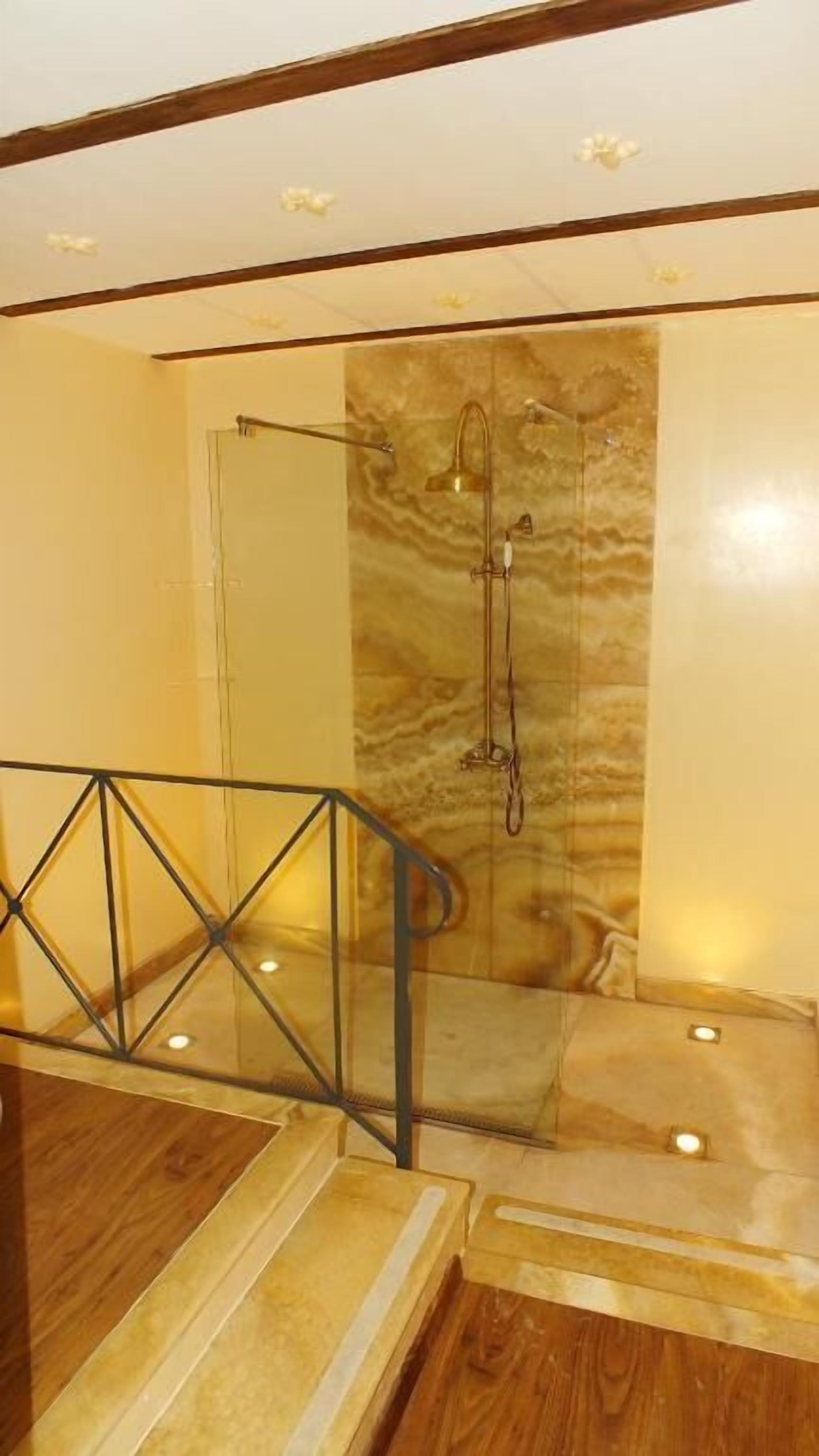 Un baño moderno con cabina de ducha de vidrio, pared de mármol y escalera de madera con barandilla de cristal.