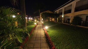 A nighttime pathway leading to a building with multiple windows and a well-lit entrance. - Hotel Palm Beach (Pointe-Noire)