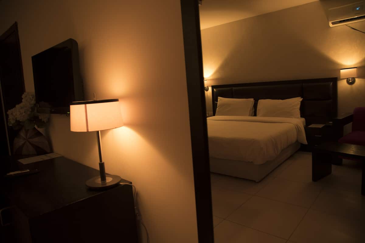 Una habitación de hotel con cama, mesita de noche, lámpara y televisión instalada en la pared.
