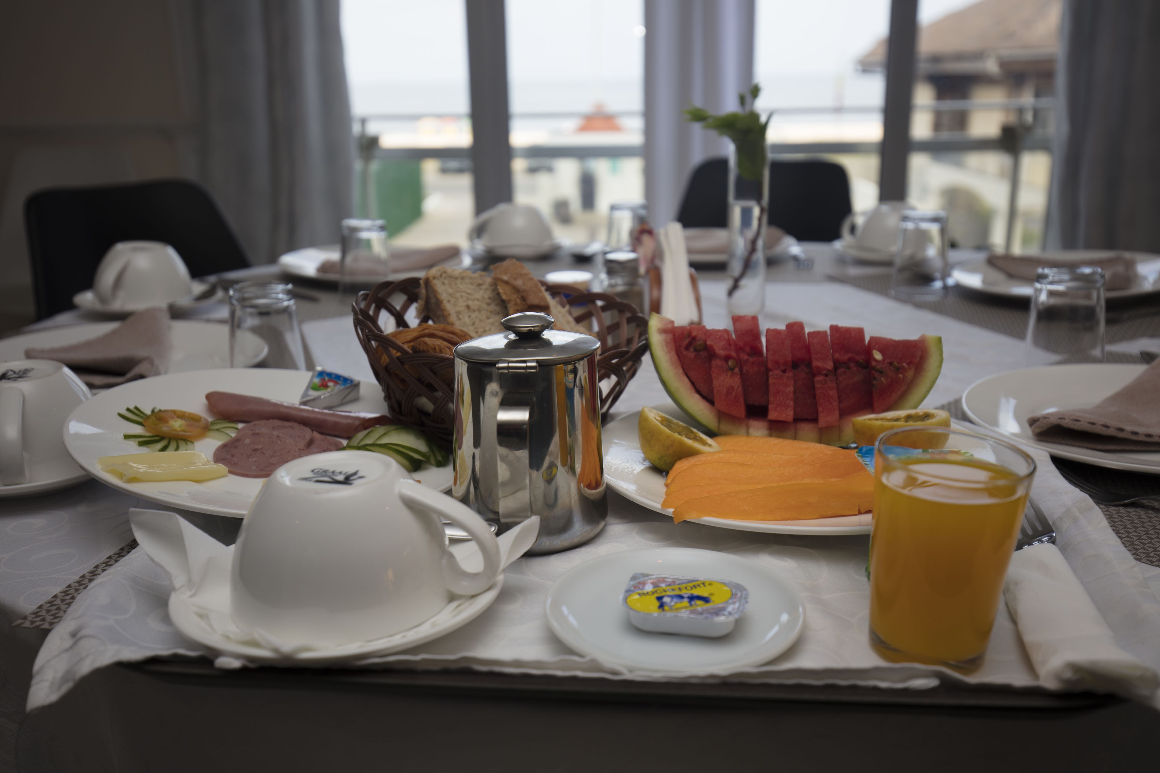A breakfast table with plates of food, a coffee pot, and a glass of juice.