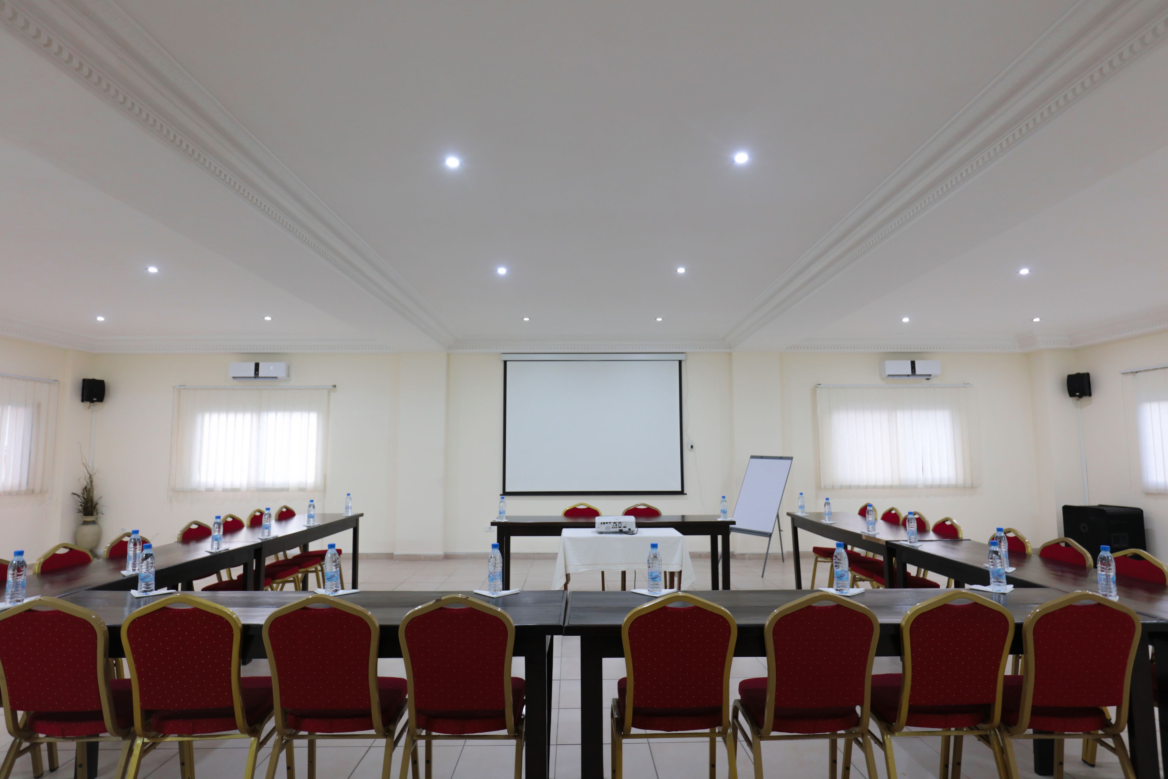 A conference room with a long table, red chairs, and a projector screen.