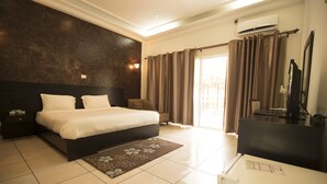 A hotel room with a large bed, a desk, a television, and a view of the outdoors. - Hotel Palm Beach (Pointe-Noire)