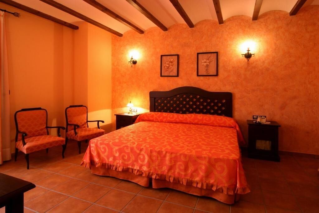 Une chambre à coucher avec un grand lit, deux chaises, une table de chevet et deux lampes fixées au mur.