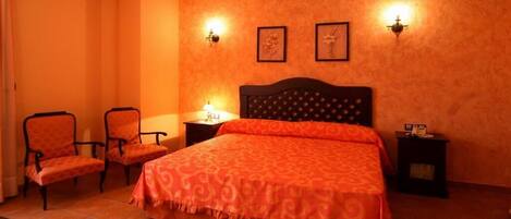 A bedroom with a large bed, two chairs, a nightstand, and two wall-mounted lamps.