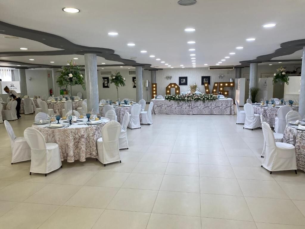 Een balzaal met ronde tafels, witte stoelen en bloemrijke decoraties.