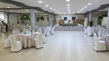 Een balzaal met ronde tafels, witte stoelen en bloemrijke decoraties.
