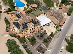 Un edificio grande con varios pisos, una piscina y una cancha de tenis.