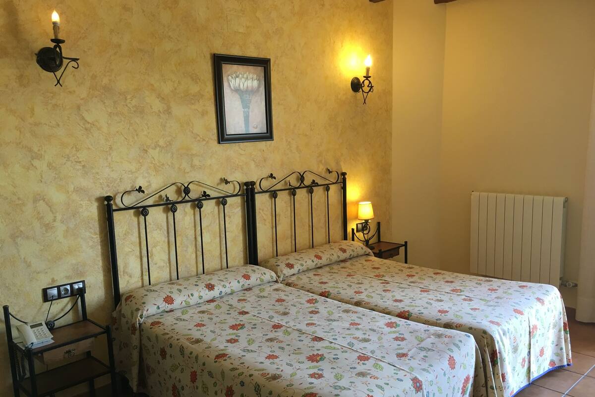 A double bed with floral bedding, a bedside table with a lamp, and a framed picture on the wall.