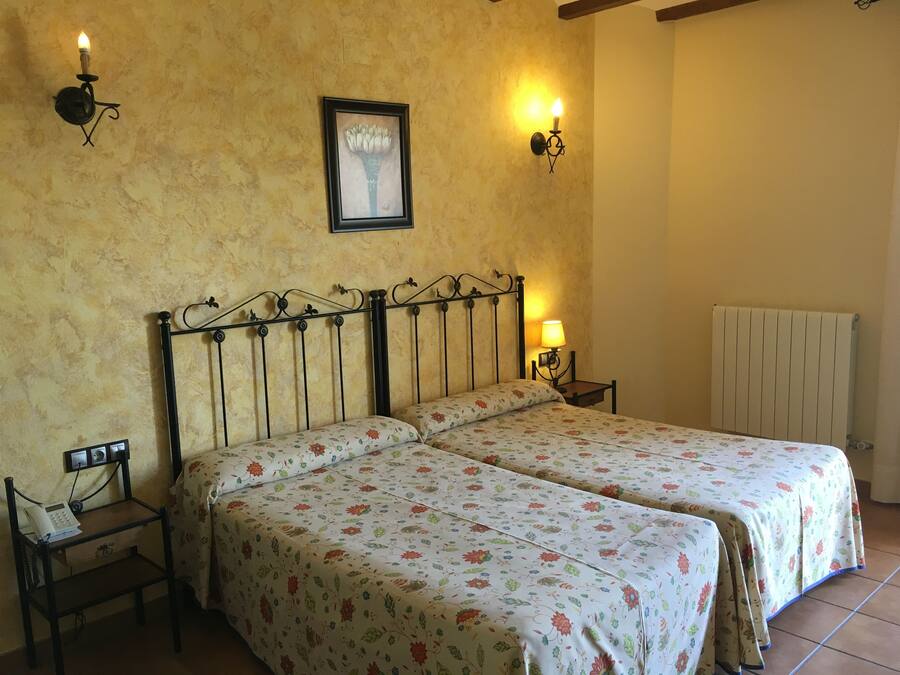 A double bed with floral bedding, a bedside table with a lamp, and a framed picture on the wall.