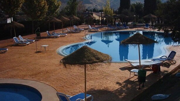 A pool area with lounge chairs and umbrellas, surrounded by trees and buildings. - Hotel rural Llano Piña (Loja)