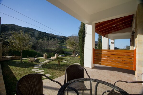 A patio area with wicker chairs, a wooden bench, and a view of a hilly landscape.