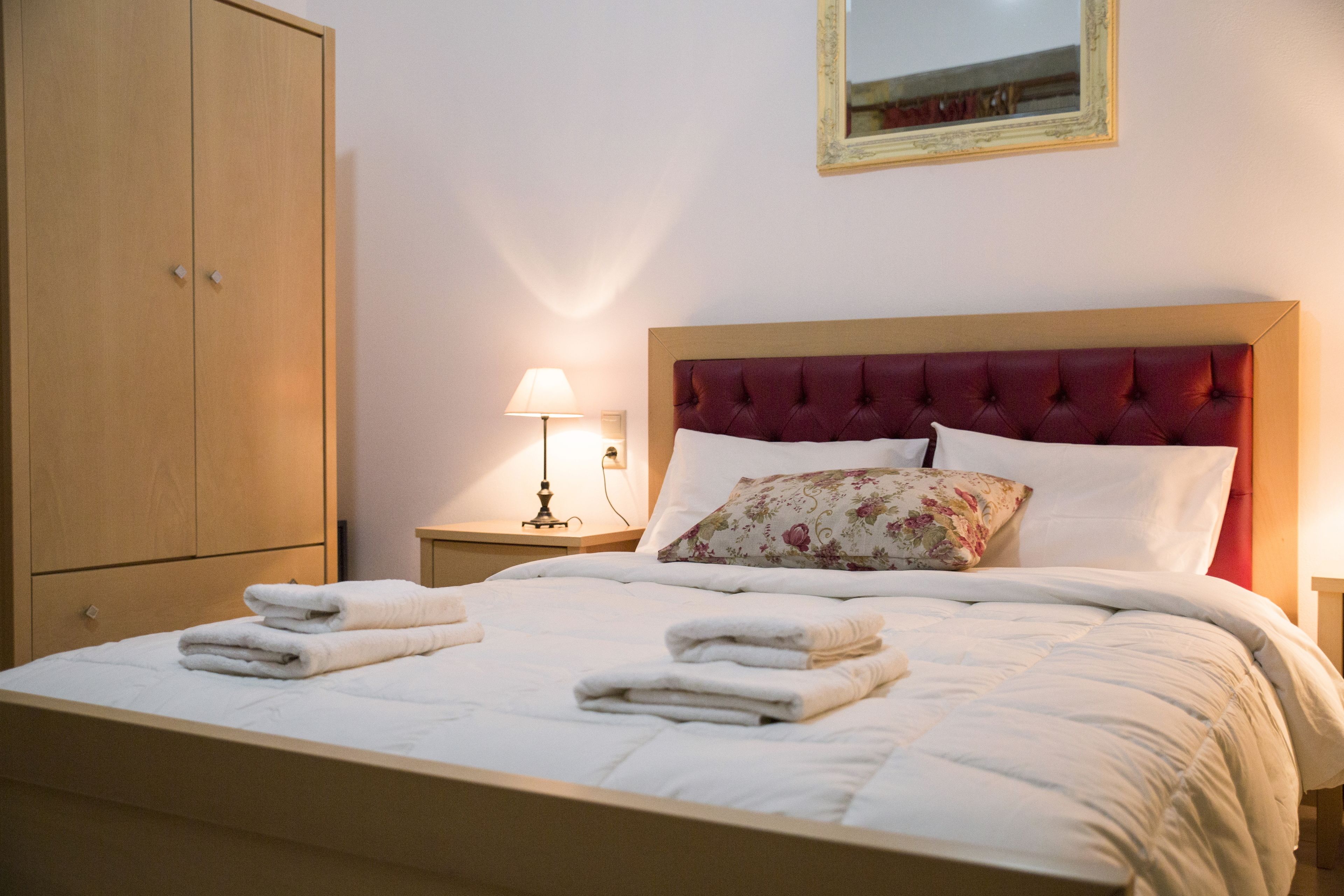 Una cama bien tendida con toallas dobladas, un armario de madera, una lámpara de noche y un espejo en la pared.