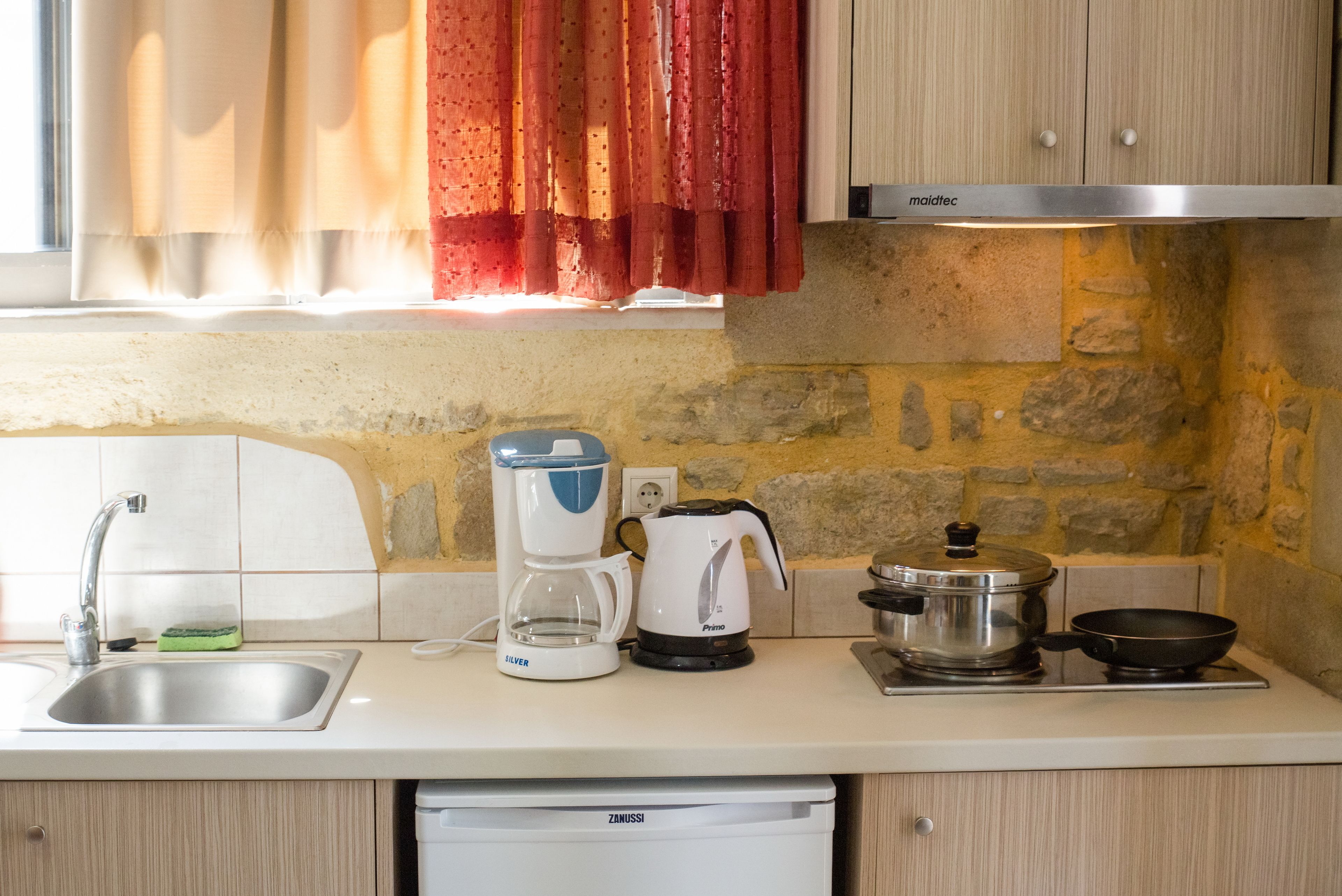 A kitchen with a sink, coffee maker, kettle, frying pan, and a dishwashing machine.