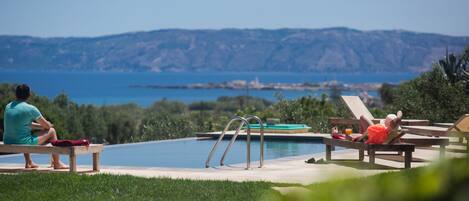 A poolside area with a view of the sea and hills, including lounge chairs and a pool.