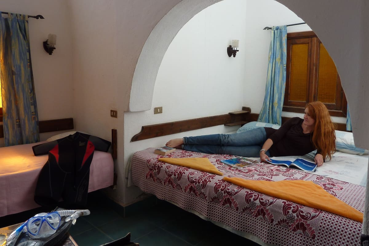 A bedroom with a bed, a small table, and a window with curtains.