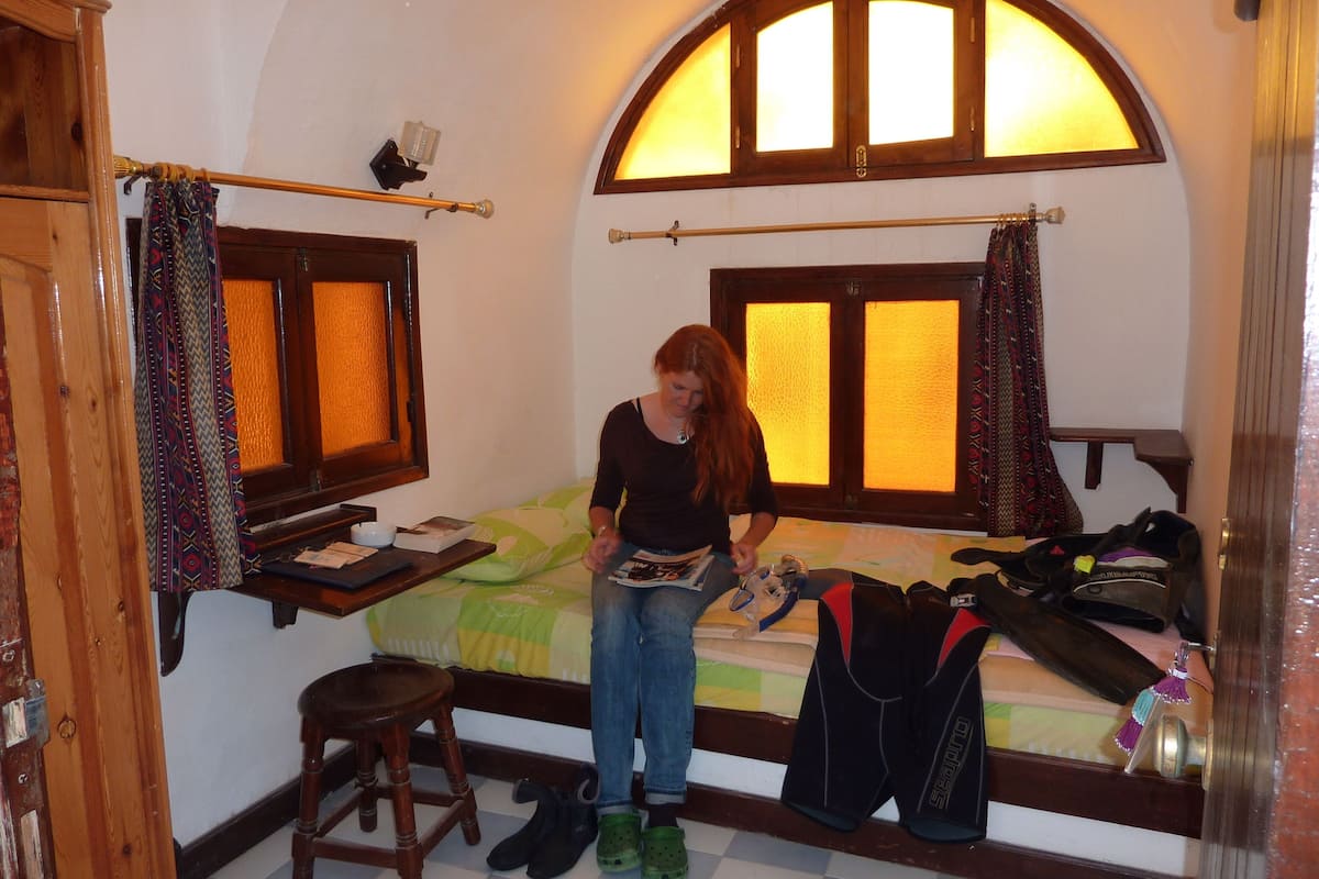 A small, cozy bedroom with a single bed, a wooden chair, and a small table.