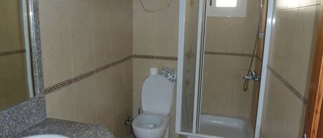 A bathroom with a granite countertop sink, a toilet, and a glass-enclosed shower.
