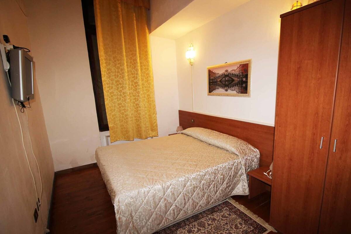 A bedroom with a bed, a wardrobe, a painting, and a lamp.