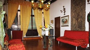 A traditional room with a red sofa, a wooden floor, a chandelier, and a large window with curtains. - Residenza Della Spada (Venice)
