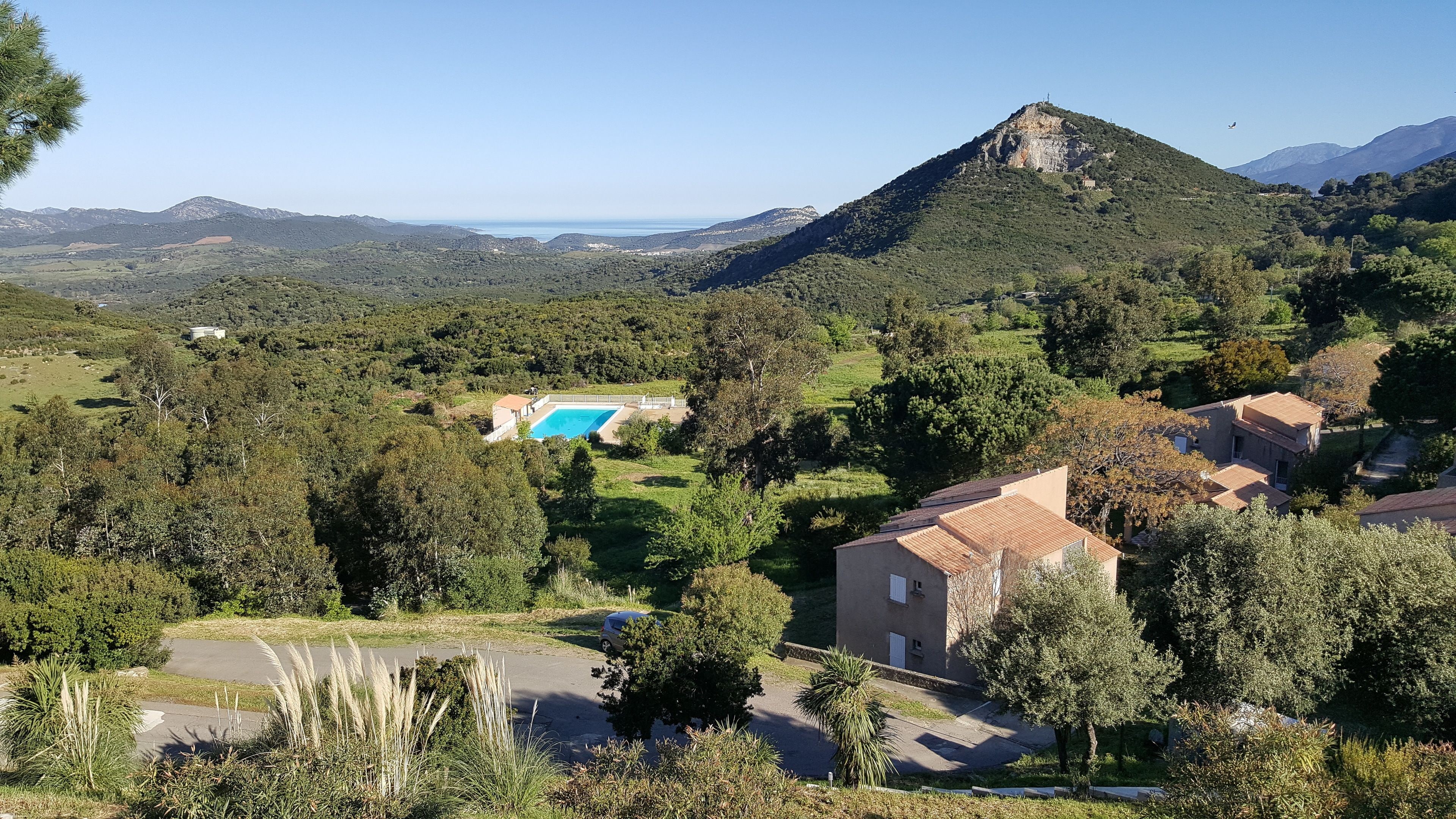 A residential area with a swimming pool, a large hill, and a clear sky.
