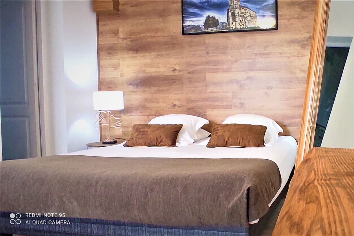 Une chambre d’hôtel avec un lit, des oreillers, une table de chevet, une lampe et un mur en bois.