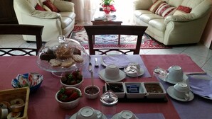 A dining table set with various food items, including bread, strawberries, and condiments, in a room with two white leather sofas and a patterned rug. - B&B Il Ghiro - Country House (Mormanno)