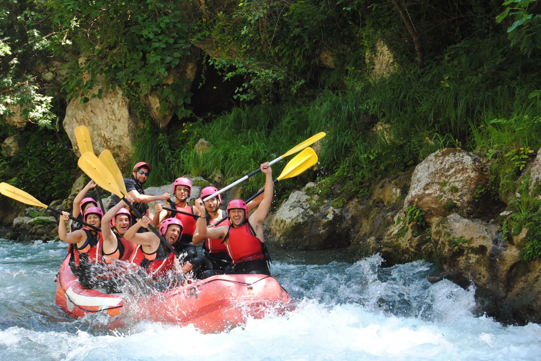 Un grupo de personas en una balsa roja navegando un río rodeado de rocas y vegetación.