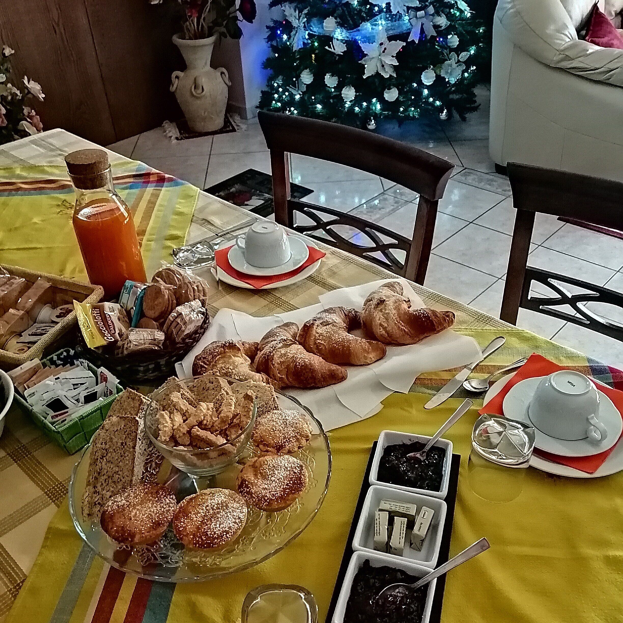 A breakfast table with pastries, a coffee pot, and a Christmas tree in the background.