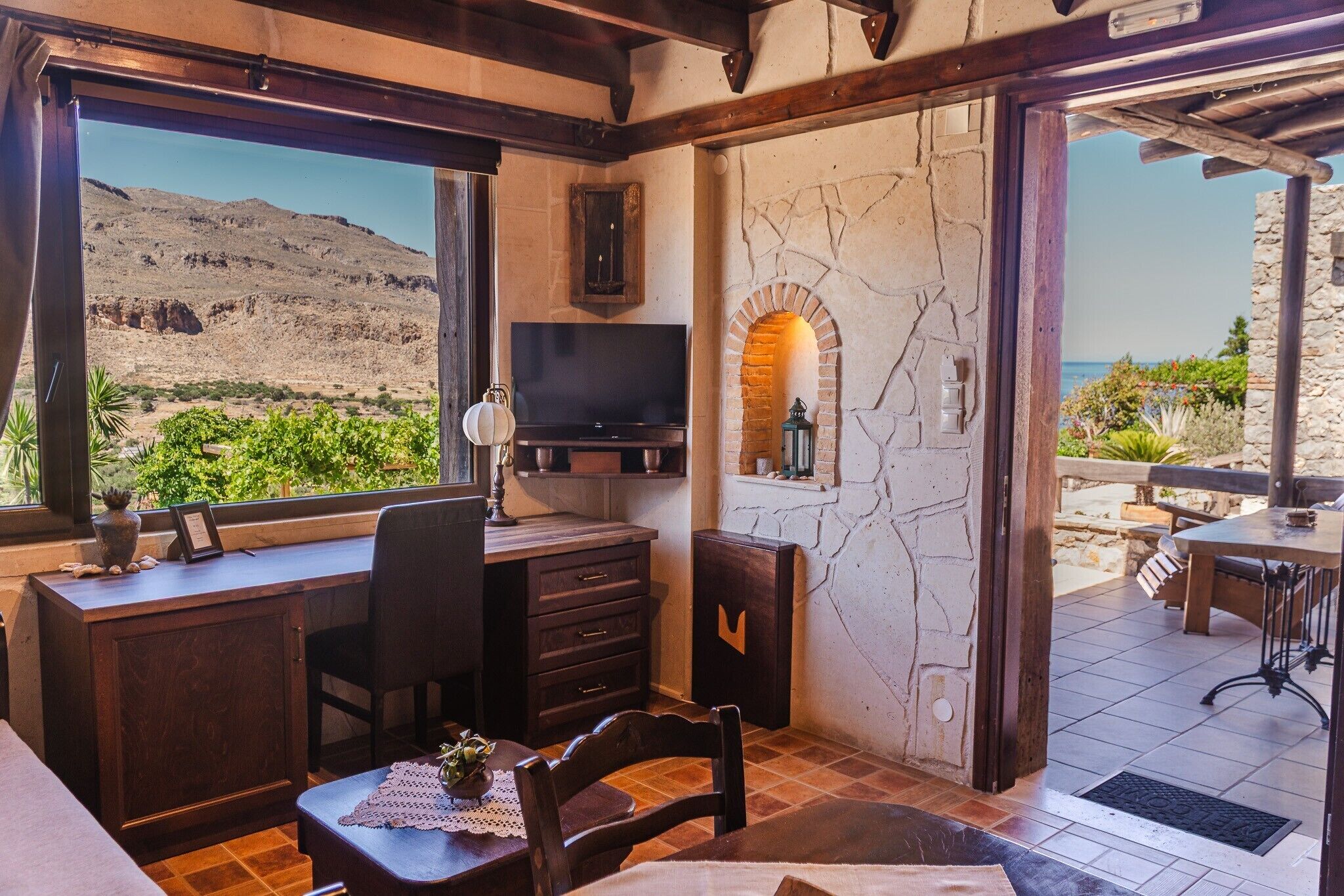A room with a TV, a desk, a chair, and a view of a mountainous landscape.
